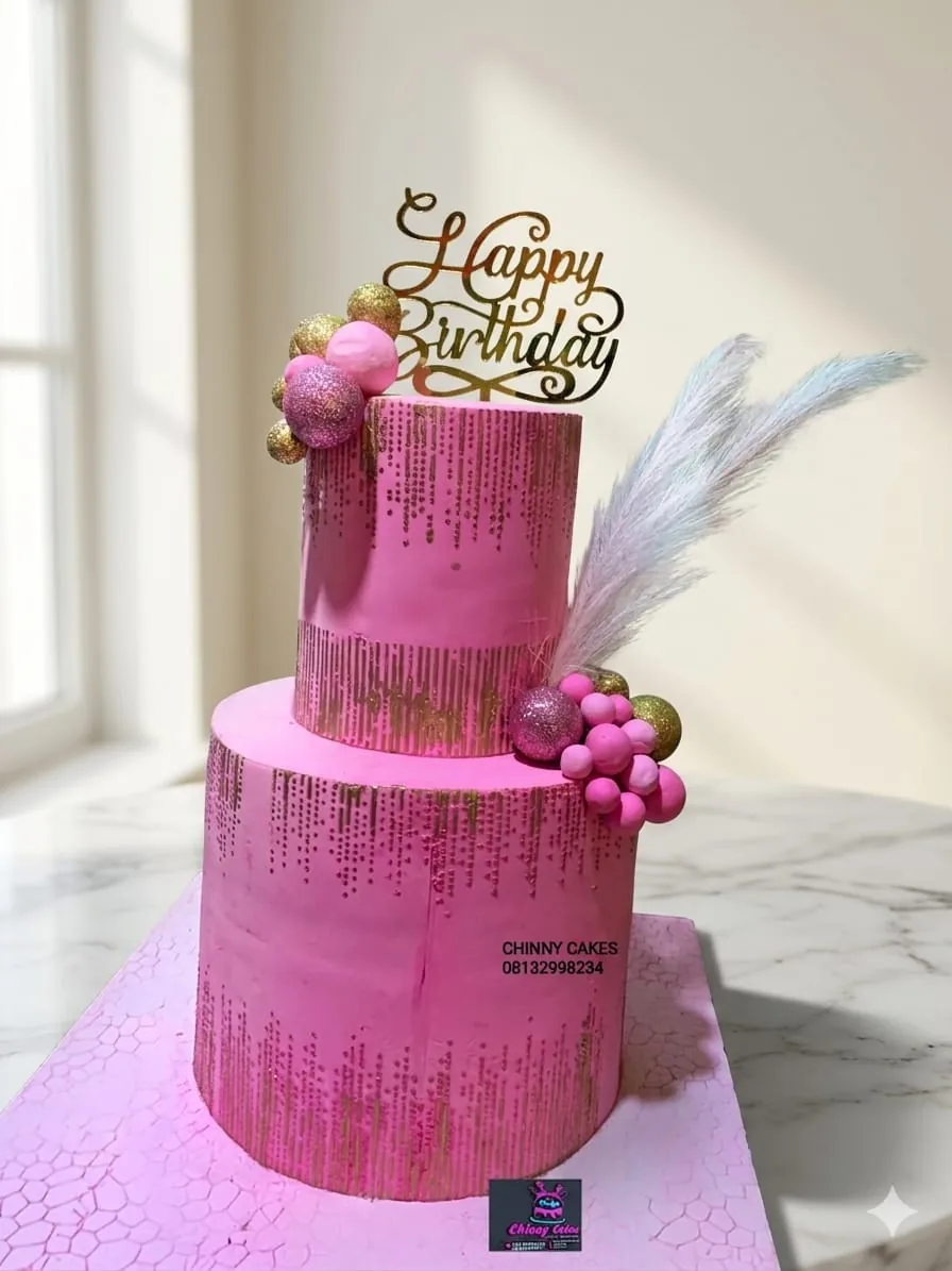 Two-tier pink birthday cake with gold detailing and decorative topper by Chinny Cakes & More