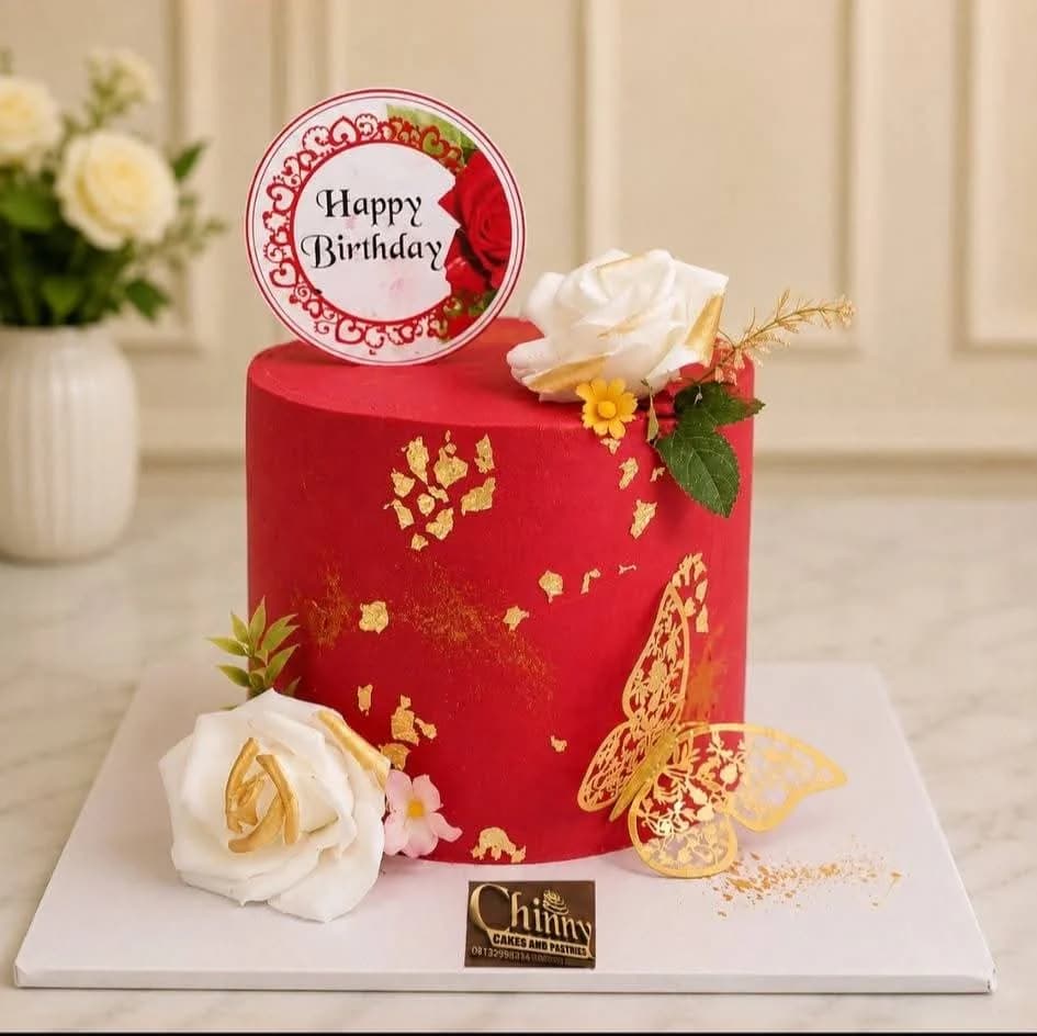 Red birthday cake with white roses, gold leaf and gold butterfly decoration